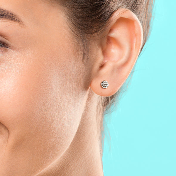 Close-up of an ear wearing a silver earring with a blue background