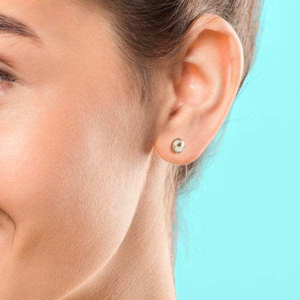 Close-up of an ear wearing a small round earring against a light blue background