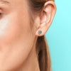 Close-up of an ear wearing a silver stud earring with a blue background