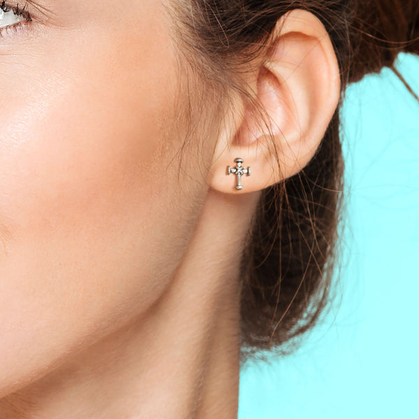 Close-up of an ear wearing a small cross earring with a blurred background