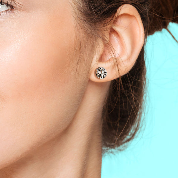 Close-up of an ear wearing a silver stud earring with a blue background