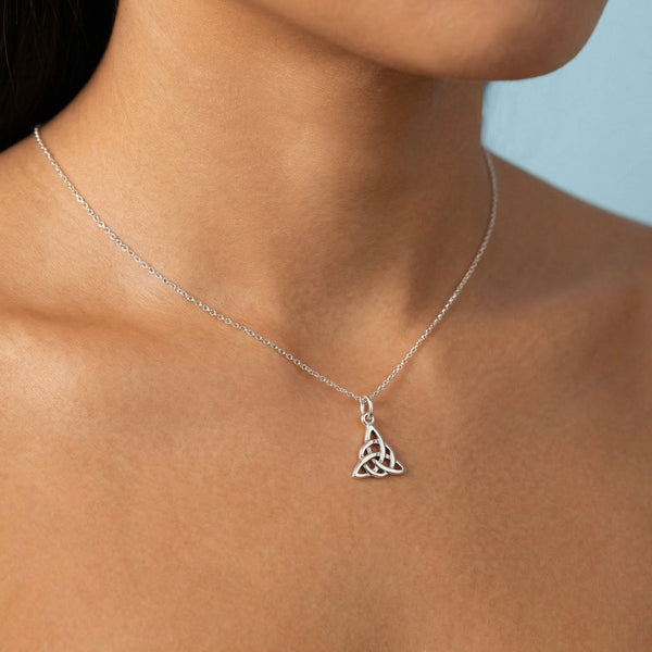 Silver necklace with a Celtic knot pendant on a person against a light blue background