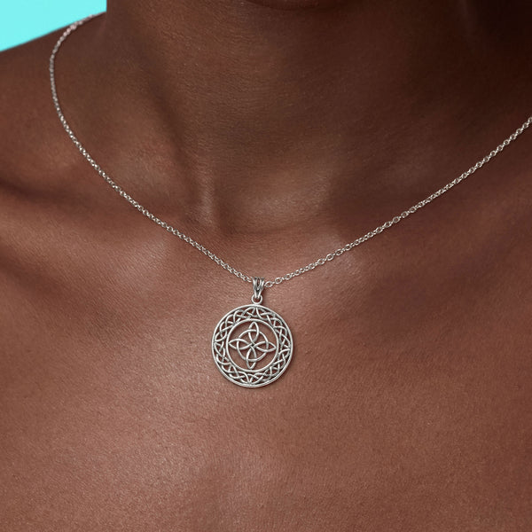 Silver necklace with a intricate pendant on a person's neck against a blue background