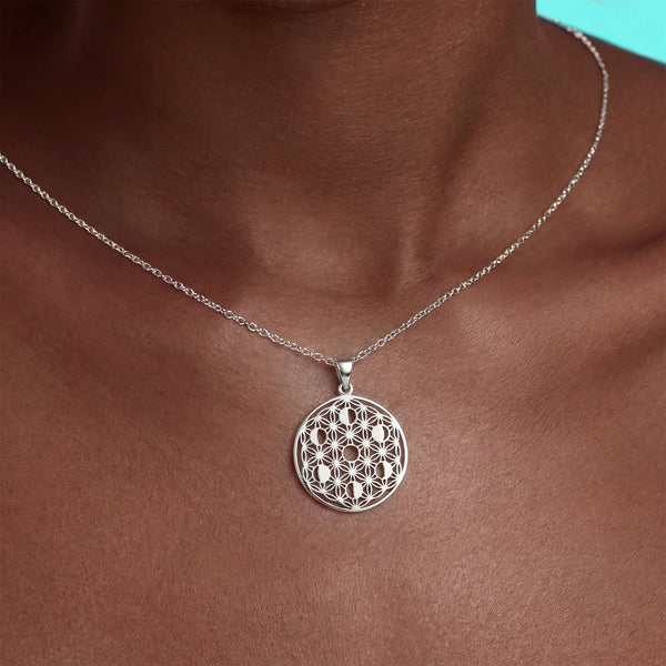 Silver necklace with a intricate pendant on a person's neck against a turquoise background