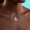 Silver necklace with a spiral pendant on a person's neck against a blue background