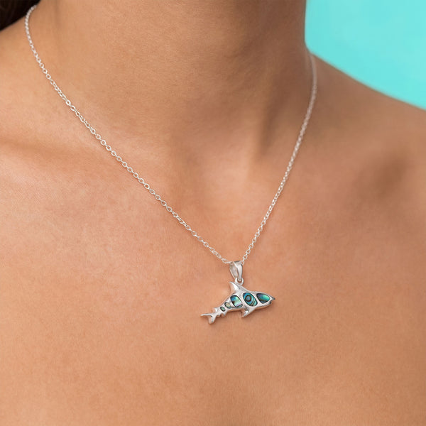 Silver shark pendant necklace on a person's neck with a turquoise background