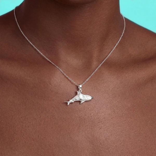 Silver shark pendant necklace on a person against a turquoise background